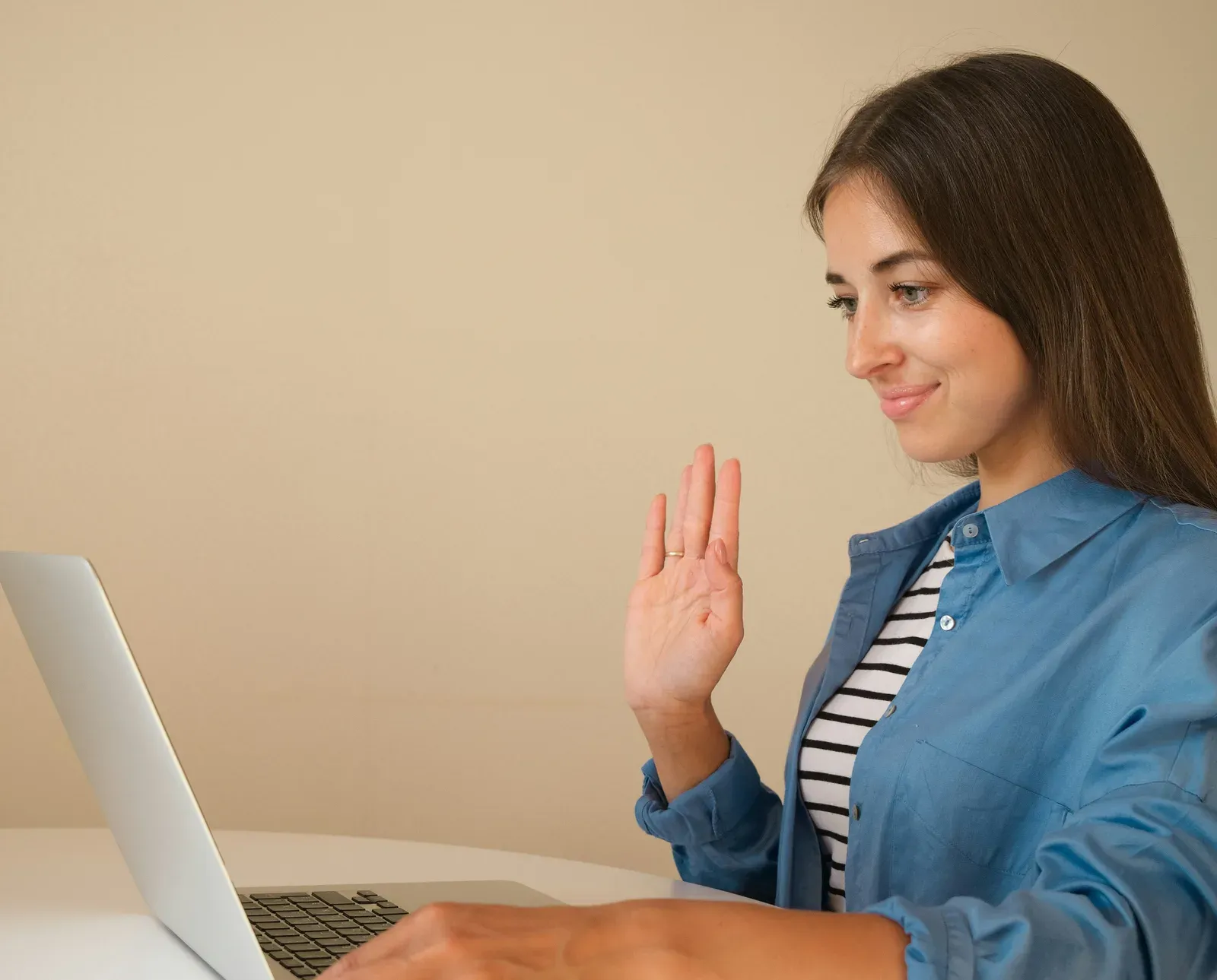 A woman smiling and waving at her laptop screen during a video call