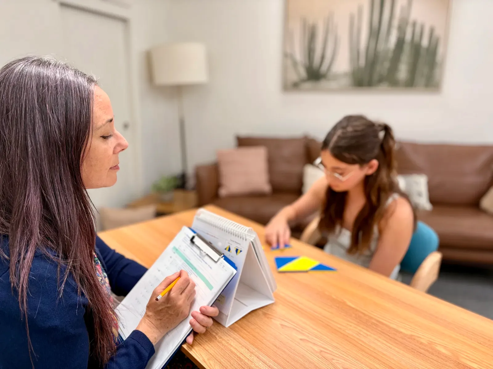 A psychologist scoring an assessment protocol while a student works through a block-design task