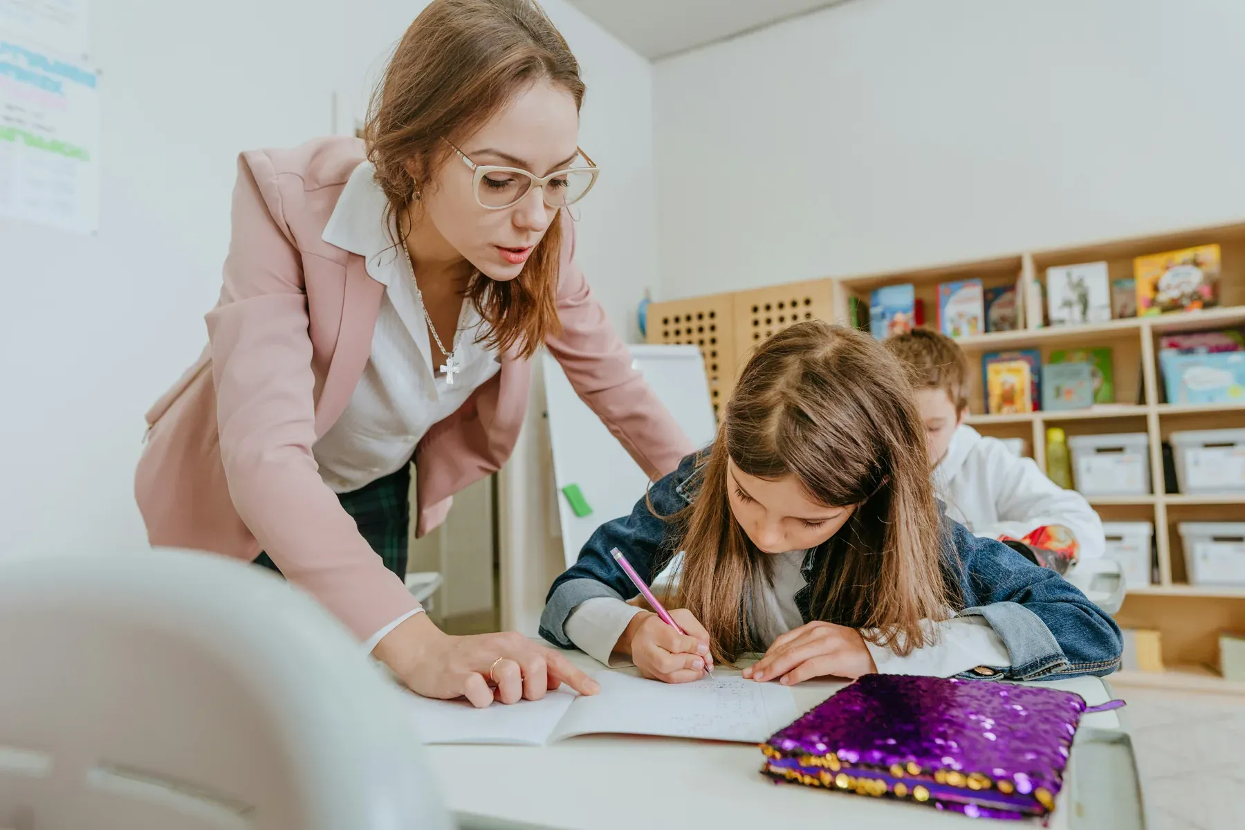 A teacher leaning over a desk to help a student with her writing